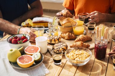 Tanımlanamayan bir grup insanın kahvaltısını ahşap bir masada birlikte yemesi. 