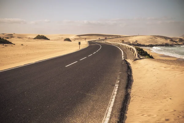 Beautiful scenic long asphalt road with desert and beach in background 