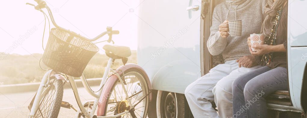 cropped view of senior couple sitting on an old vintage van together drinking tea or coffee