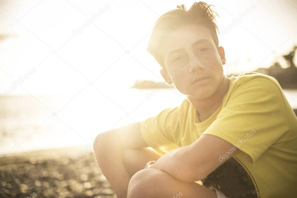 Beautiful portrait young handsome people male teenager looking at the camera sitting at the beach with sunset sun in back light 