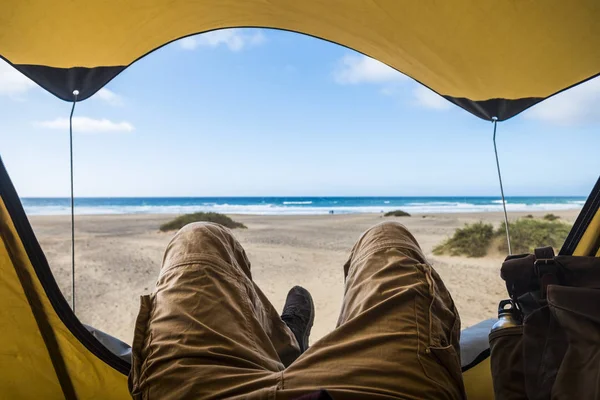 Point of view with laying man inside a tent enjoying relax and adventure in free camping with beach and sea