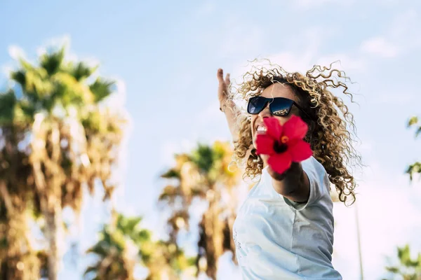 blonde curly beautiful people adult woman jumping and showing a big red flowers at the camera