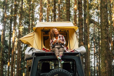 Seyahat ve gezgin yaşam tarzı konsepti. Mutlu, yalnız, yetişkin bir kadın. Arka planda ahşap ormanlarla dolu bir arabada oturur ve doğa ve açık havada tatilin tadını çıkarır.