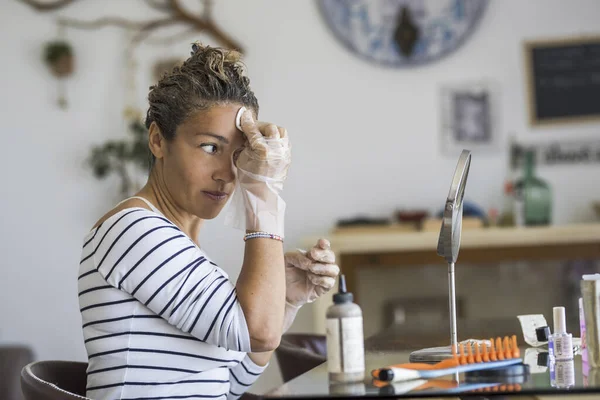 Home made hair dye at home for beauty young caucasian woman looking at the mirror - stay at home concept for coronavirus emergency worldwide pandemic contagion