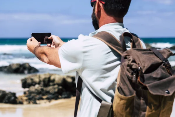 Stojący Człowiek Plecakiem Oglądany Tyłu Zrobić Zdjęcie Wybrzeżu Morza Smartfonem — Zdjęcie stockowe