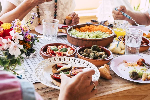 家やレストランで友情や友情で一緒に食べる人々のグループと新鮮な菜食主義者の食べ物でいっぱいのテーブルの近くに — ストック写真