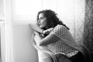 Evde oturan ve pencereden ışığa bakan genç bir kadın için yalnızlık ve depresyon hastalığı kavramı. Kız evde üzgün üzgün oturuyor.