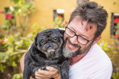Açık havada, siyah sakallı beyaz bir adamın güzel portresi ve arka planda eski komik köpek pug - arka planda bahçe ve en iyi arkadaş aşk konsepti