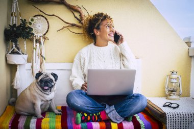 Komik iş ve teknoloji konsepti resmi. Yetişkin, neşeli, beyaz, güzel bir kadın telefonla arıyor ve dizüstü bilgisayar kullanıyor. Yanında sevimli, sevimli, sevimli bir köpek pug arkadaşı var.