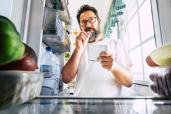 大人Caucasian男取りますノートリストの食品見中にザオープン冷蔵庫で自宅 — ストック写真