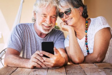 Mutlu, güzel, yaşlı çift, modern online teknoloji cihazıyla bir telefon görüşmesi yapıyor. Sevgi ve dostlukla emekli insanlar. Kafkasyalı yetişkinler ve internet bağlantısı.