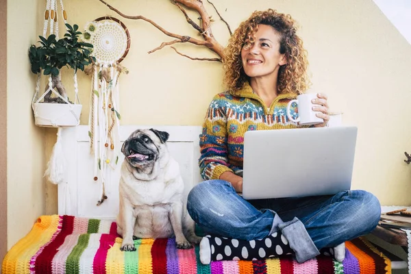 Happy couple woman and funny dog at home sitting on a coloured cover have fun and use technology laptop computer - lockdown and home office smart work job lifestyle