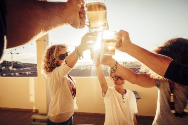 Karışık çağ ve nesiller boyu, evde bira ve meyve suyuyla birlikte, arka planda güneş ışığı olan terasta kadeh kaldırılır. Dostluk ve kutlama insanları kavramı.