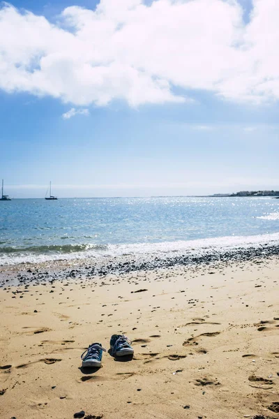 青い海の水の近くのビーチで 美しい空の下で砂の上の靴のペアで観光や夏休みのコンセプト — ストック写真