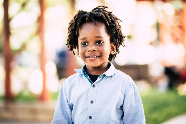 Beutiful black african people children portrait with park outdoor defocused background - color and skin race diversity child concept with cheerful kid smiling and be happy - alternative dreadlocks hair