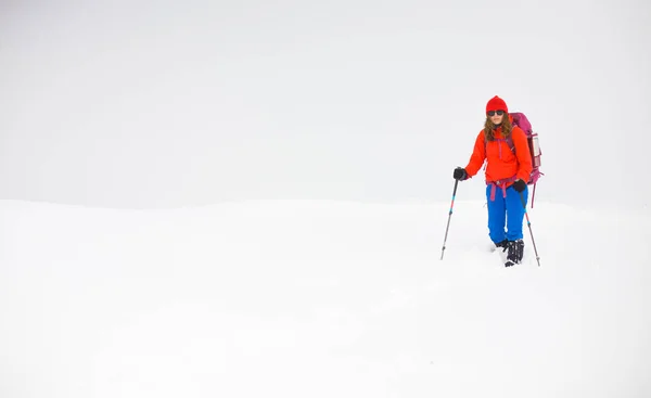 Flicka med ryggsäck gå på snö i bergen. — Stockfoto