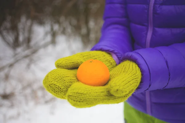 Mãos femininas em mitenes segurando uma tangerina . — Fotografia de Stock