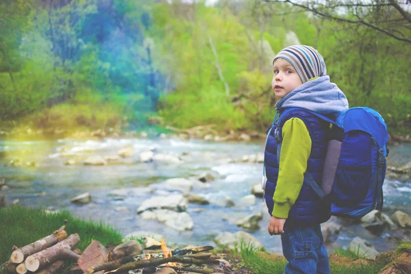 Ein Junge mit einem Rucksack steht am Ufer des Flusses. — Stockfoto
