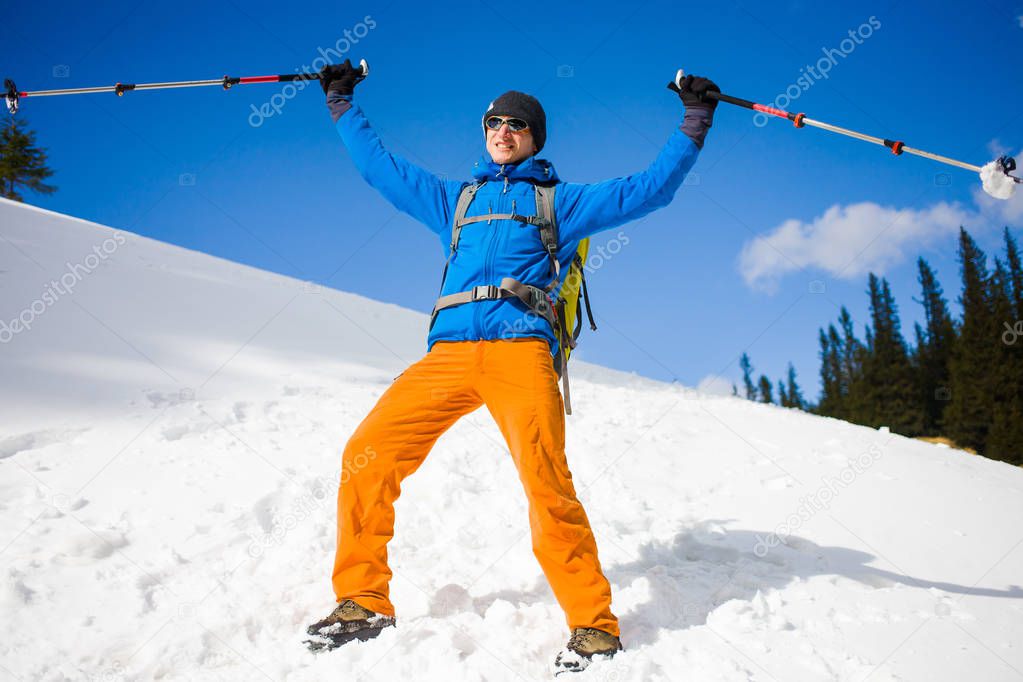 Man with trekking poles goes through the snow in the mountains.