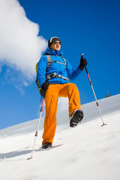 Homem com postes de trekking atravessa a neve nas montanhas . — Fotografia de Stock