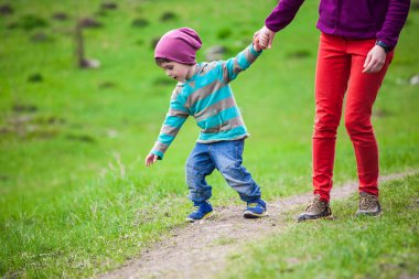 Çocuk annesiyle çayır aracılığıyla yürüyor.