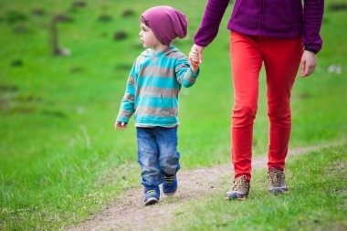 Çocuk annesiyle çayır aracılığıyla yürüyor.