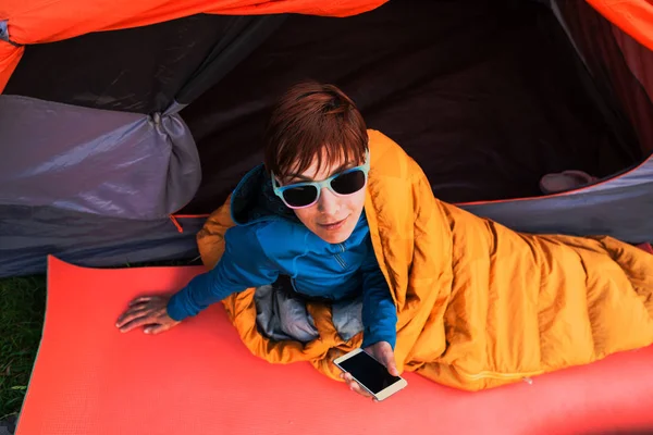 Menina com um telefone em um saco de dormir . — Fotografia de Stock