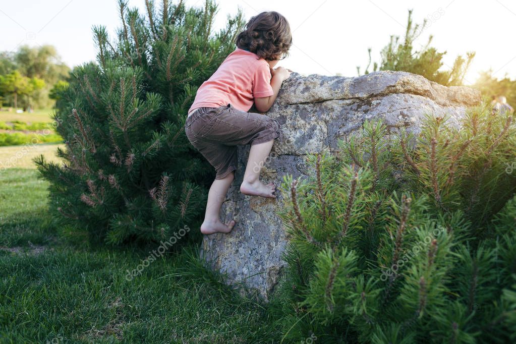 The boy climbs on the stone.