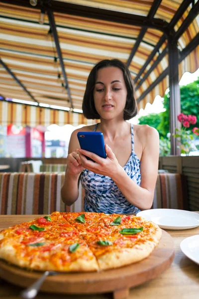 Девушка делает фото пиццы по телефону. . — стоковое фото