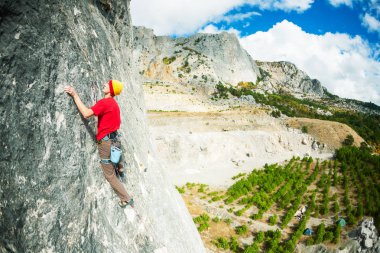 Bir kayanın üzerinde şapkalı bir dağcı.