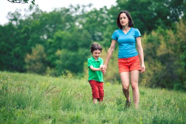 Çocuk annesiyle çayır yürür.