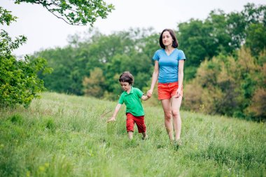 Çocuk annesiyle çayır yürür.