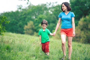 Çocuk annesiyle çayır yürür.