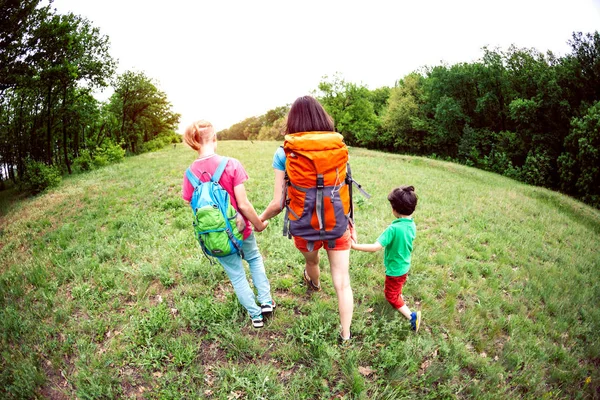 A woman with children goes hiking. The woman took her sons by the arms. Traveling with family. The boy walks with his brother and mother in the forest. Hike with backpacks.