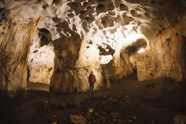 A woman with a backpack stands in the middle of the cave.