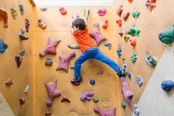 Chłopiec wspinaczka na sztuczne głazy ściany w siłowni — Zdjęcie stockowe