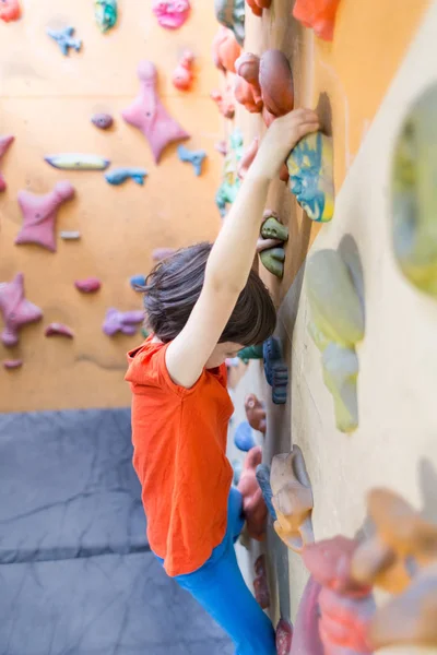 Мальчик забирается на стены искусственных валунов в спортзале — стоковое фото