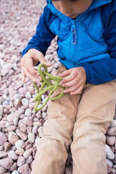 Un niño aprende a tejer un nudo de una cuerda . — Foto de Stock