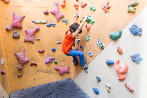 Garçon escalade sur mur de blocs artificiels dans la salle de gym — Photo