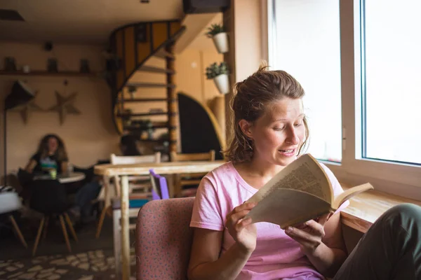 Una mujer está leyendo un libro cerca de la ventana . — Foto de Stock