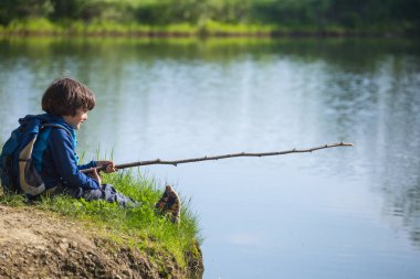 Sırt çantası olan bir çocuk tahta bir sopayla gölde oturuyor..