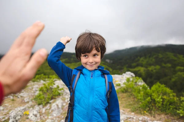 リュックサックを持った少年が山の頂上に登り、5人を与える. — ストック写真