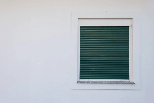 White plastic window with green shutters.