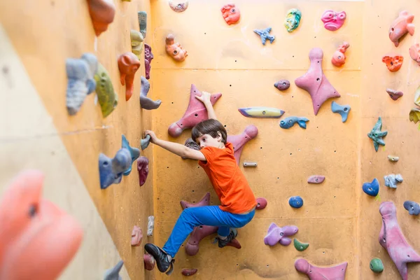 Мальчик забирается на стены искусственных валунов в спортзале — стоковое фото