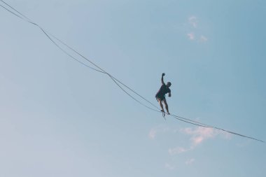 Mavi gökyüzünün arka planındaki Highliner bir hamle yapar. Bir adam uzatılmış bir askıda yürüyor. Performans ipi yürüteç. İnsan, abyss üzerinde dengeler. İleriye doğru kararlı bir adım.