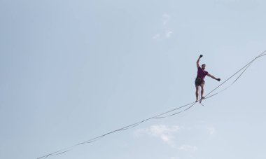 Mavi gökyüzünün arka planındaki Highliner bir hamle yapar. Bir adam uzatılmış bir askıda yürüyor. Performans ipi yürüteç. İnsan, abyss üzerinde dengeler. İleriye doğru kararlı bir adım.