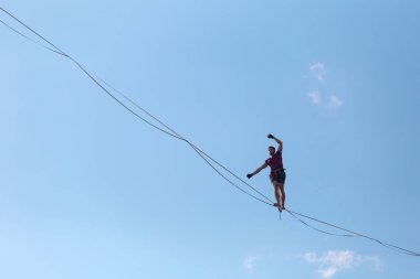 Mavi gökyüzünün arka planındaki Highliner bir hamle yapar. Bir adam uzatılmış bir askıda yürüyor. Performans ipi yürüteç. İnsan, abyss üzerinde dengeler. İleriye doğru kararlı bir adım.