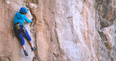 Miğferli bir kadın güzel bir turuncu kayaya tırmanıyor. Koruyucu ekipmana tırmanıyorum. Tırmanırken güvenlik. Kaya tırmanışçısı doğal bir arazide zorlu bir rotanın üstesinden gelir. Türkiye 'de kaya tırmanışı.