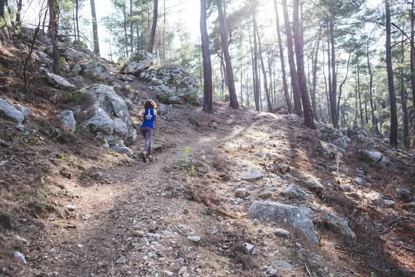 A woman runs along a mountain trail. Runner is training in the forest. Girl jogging in the park. Skyrunning.