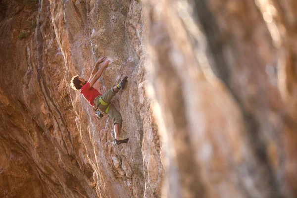 A strong man climbs a cliff. Climber overcomes a difficult climbing route on a natural terrain. Rock climbing in Turkey. Beautiful orange rock.